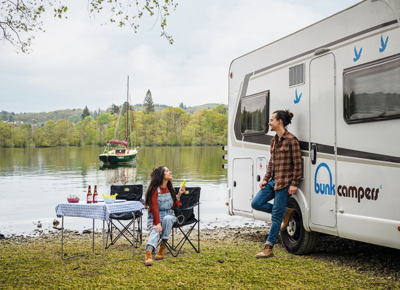 couple sitting by lake next to motorhome