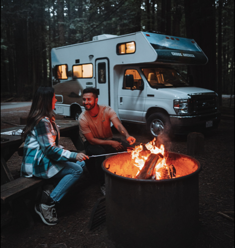man and woman enjoying bonfire next to cruise america rv